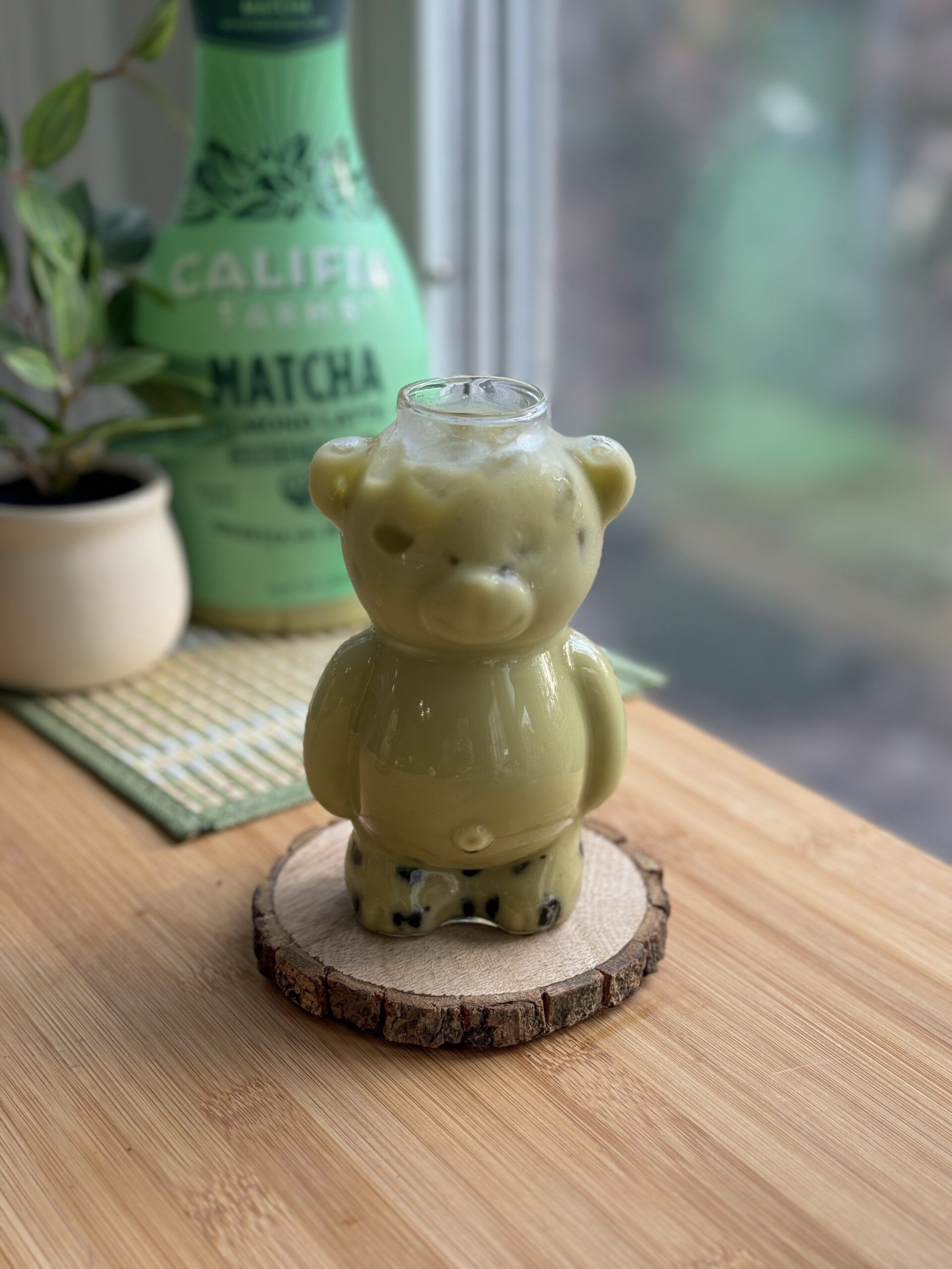 A bear-shaped glass sits at the front of the image, filled with an iced matcha latte with boba pearls