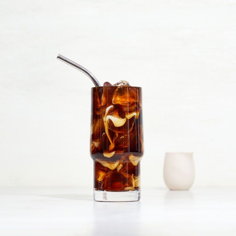 a glass of iced coffee with creamer mixing in