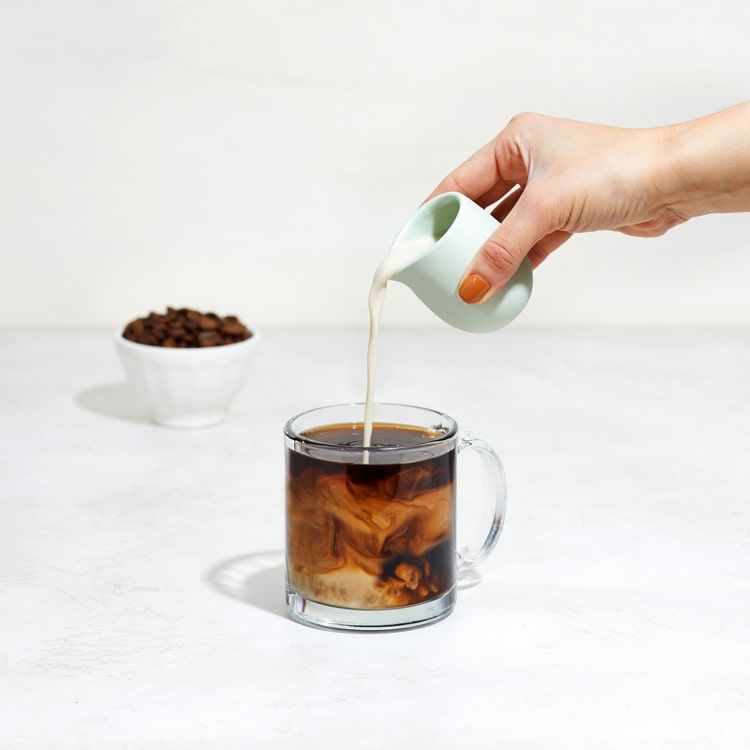 oat milk being poured in a mug of coffee