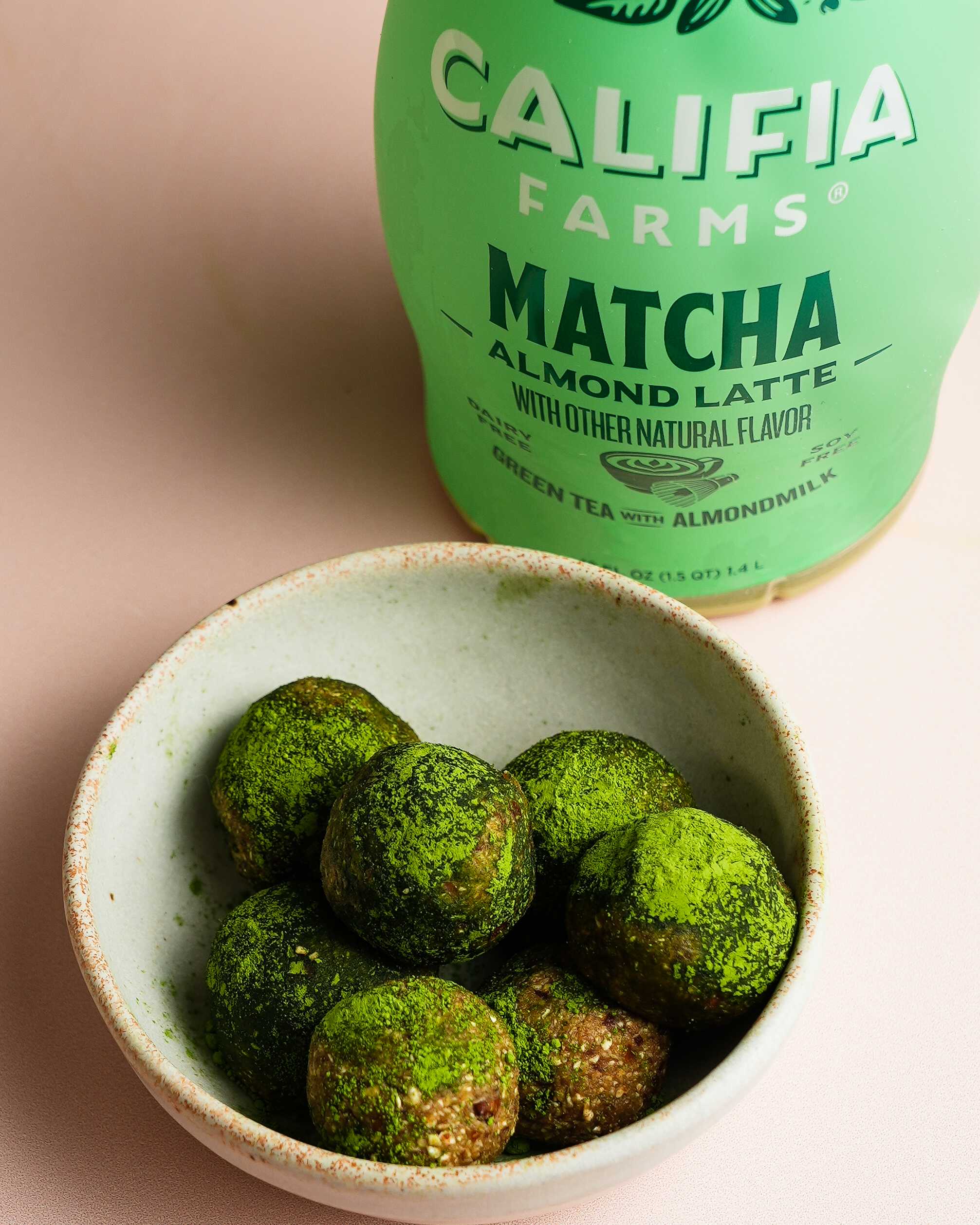 Homemade matcha energy balls sit in a bowl at the front of the image, with Califia Farms Matcha Latte in the background.