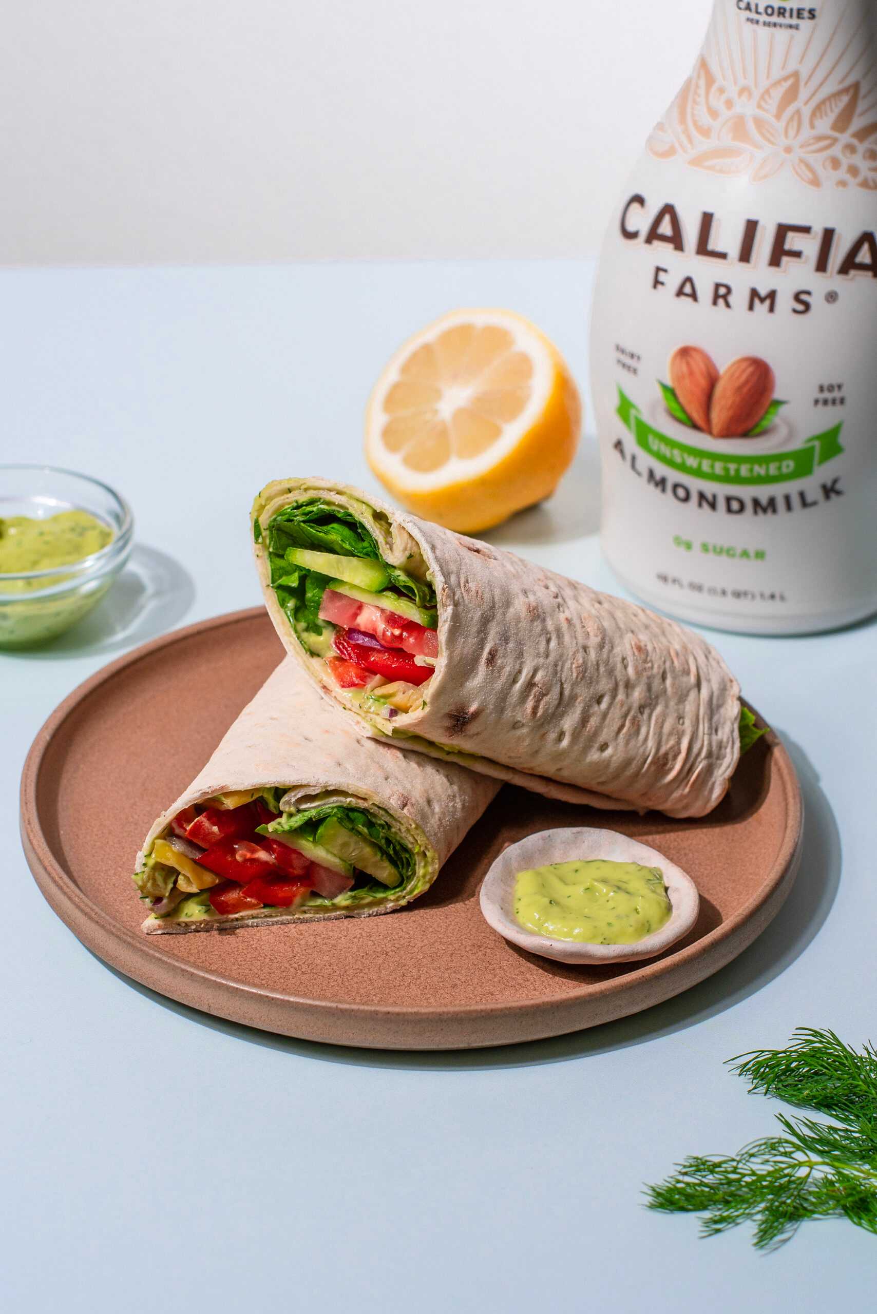 Veggie flatbread wraps sit in the center of the image with Califia Farms Unsweetened Almondmilk in the background.
