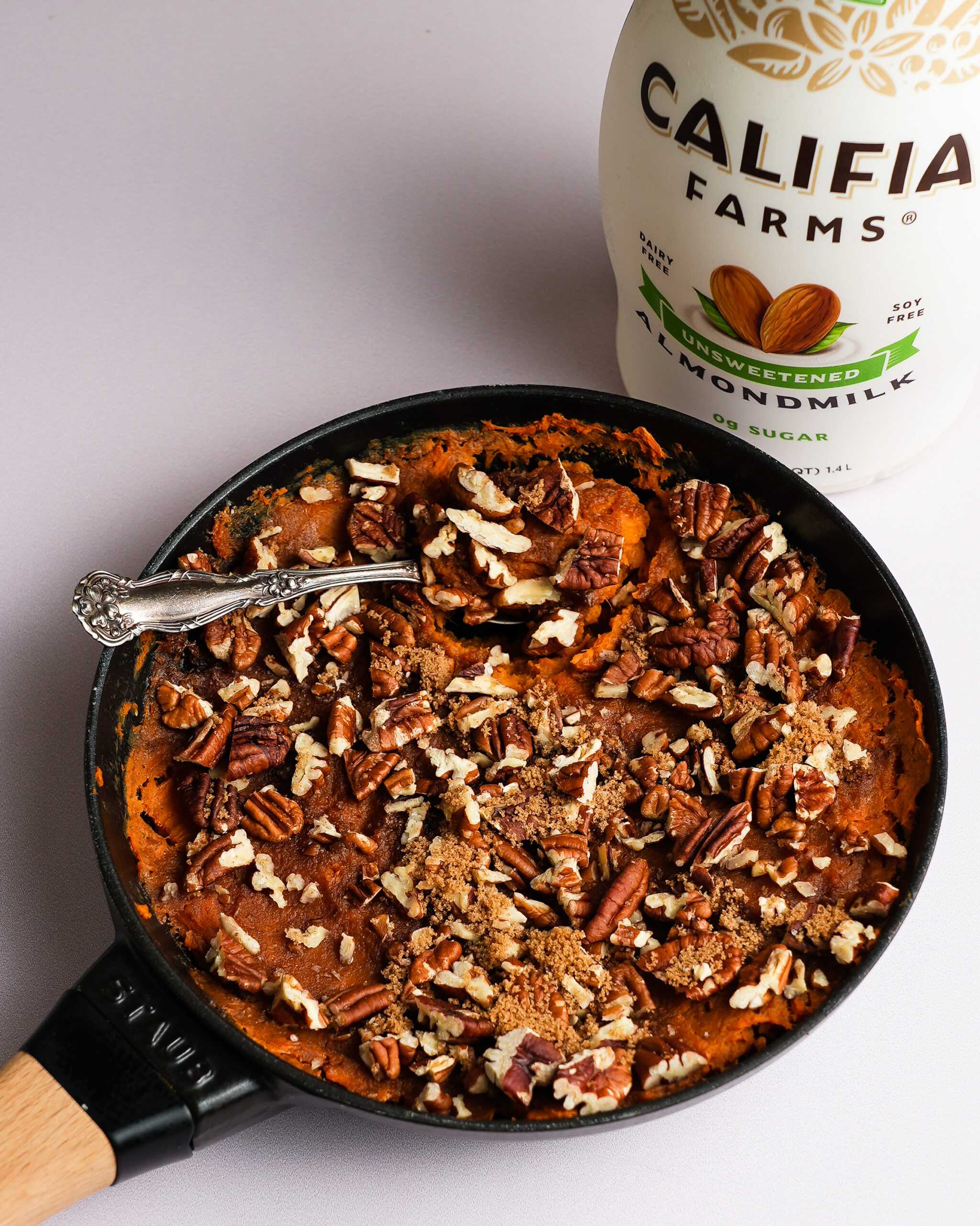 Sweet potato casserole topped with pecans sits at the foreground of the image, with Califia Farms Unsweetened Almondmilk behind.