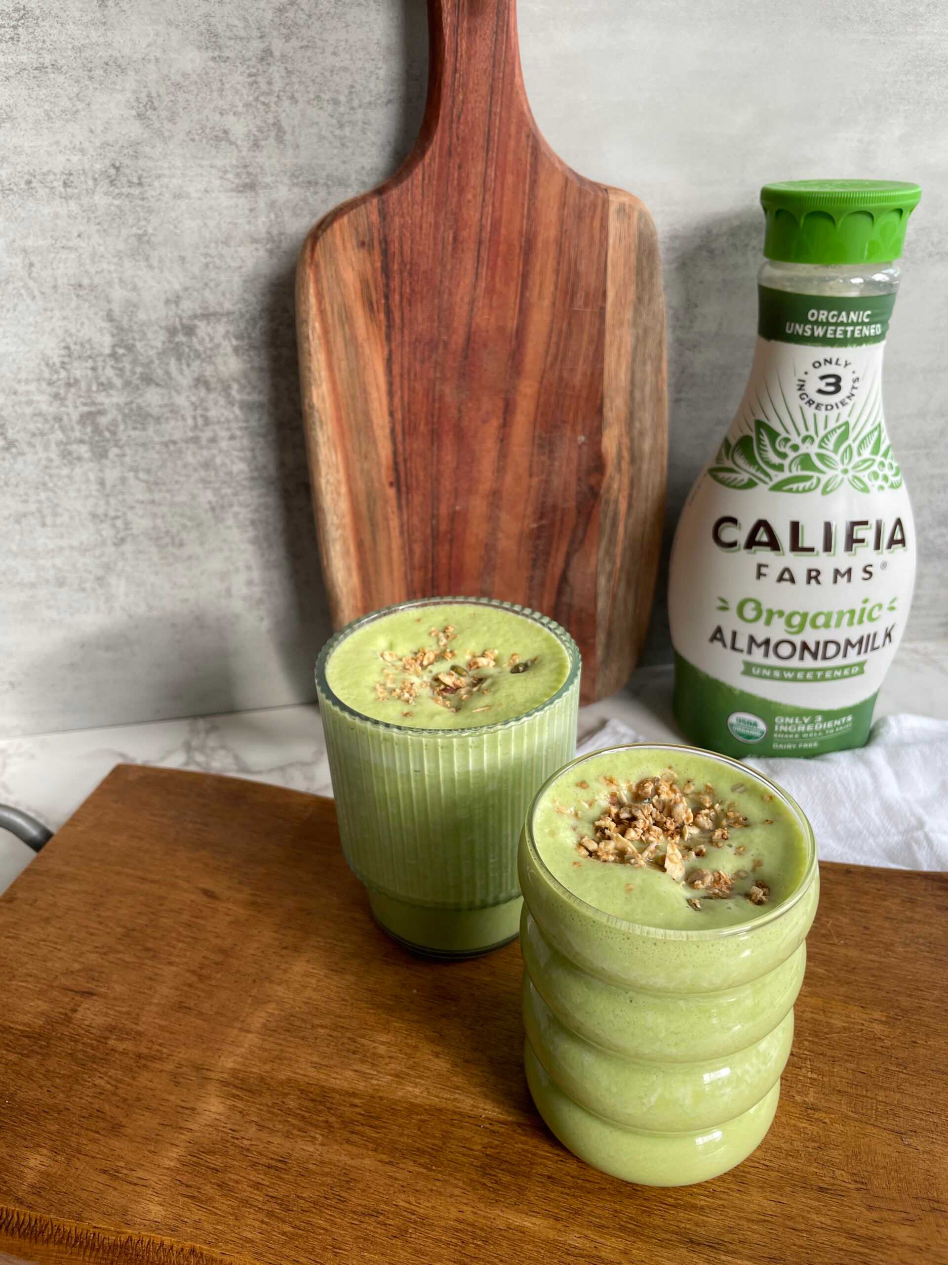 Two glasses filled with a green smoothie sit at the forefront of the image, with Califia Farms Organic Almondmilk behind.