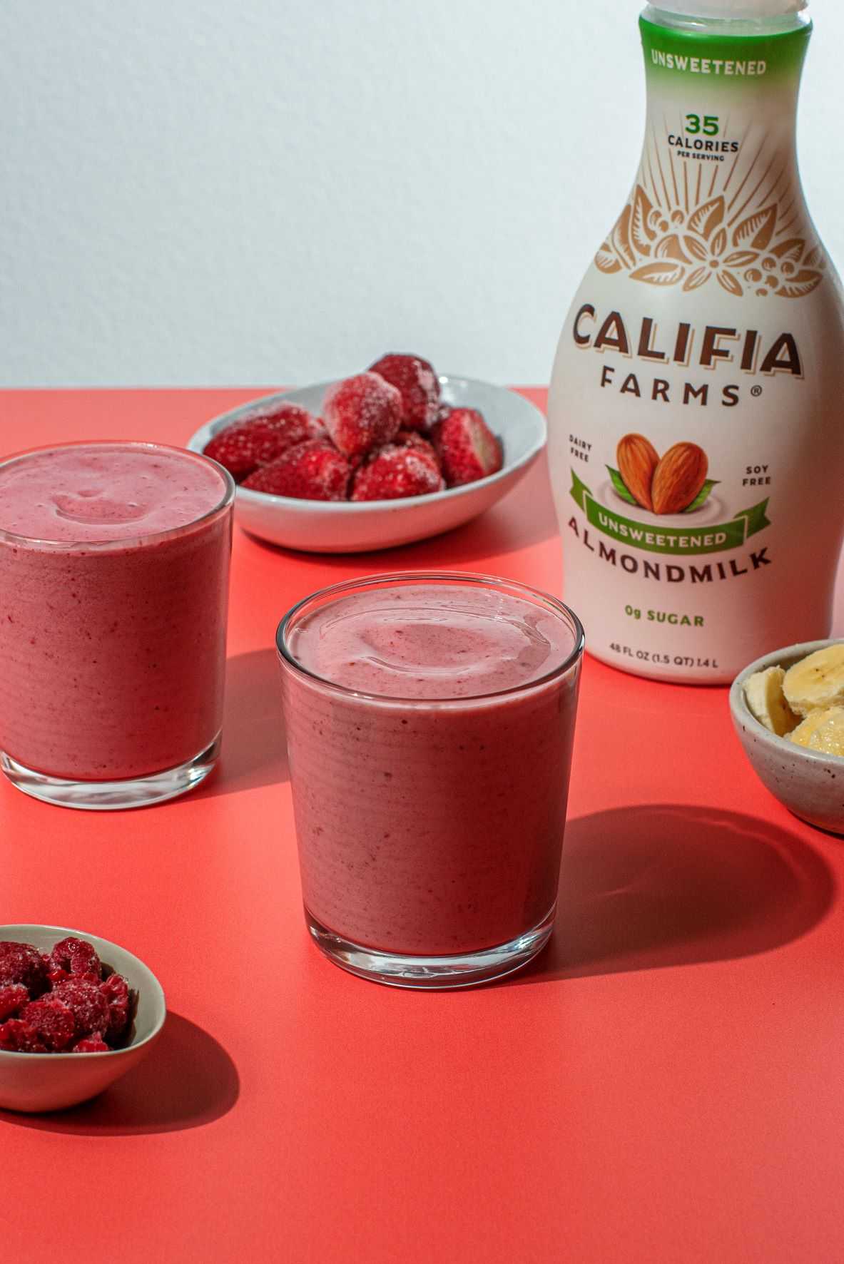 Smoothie sits in a glass at the center of the image with Califia Farms Unsweetened Almondmilk off to the side.