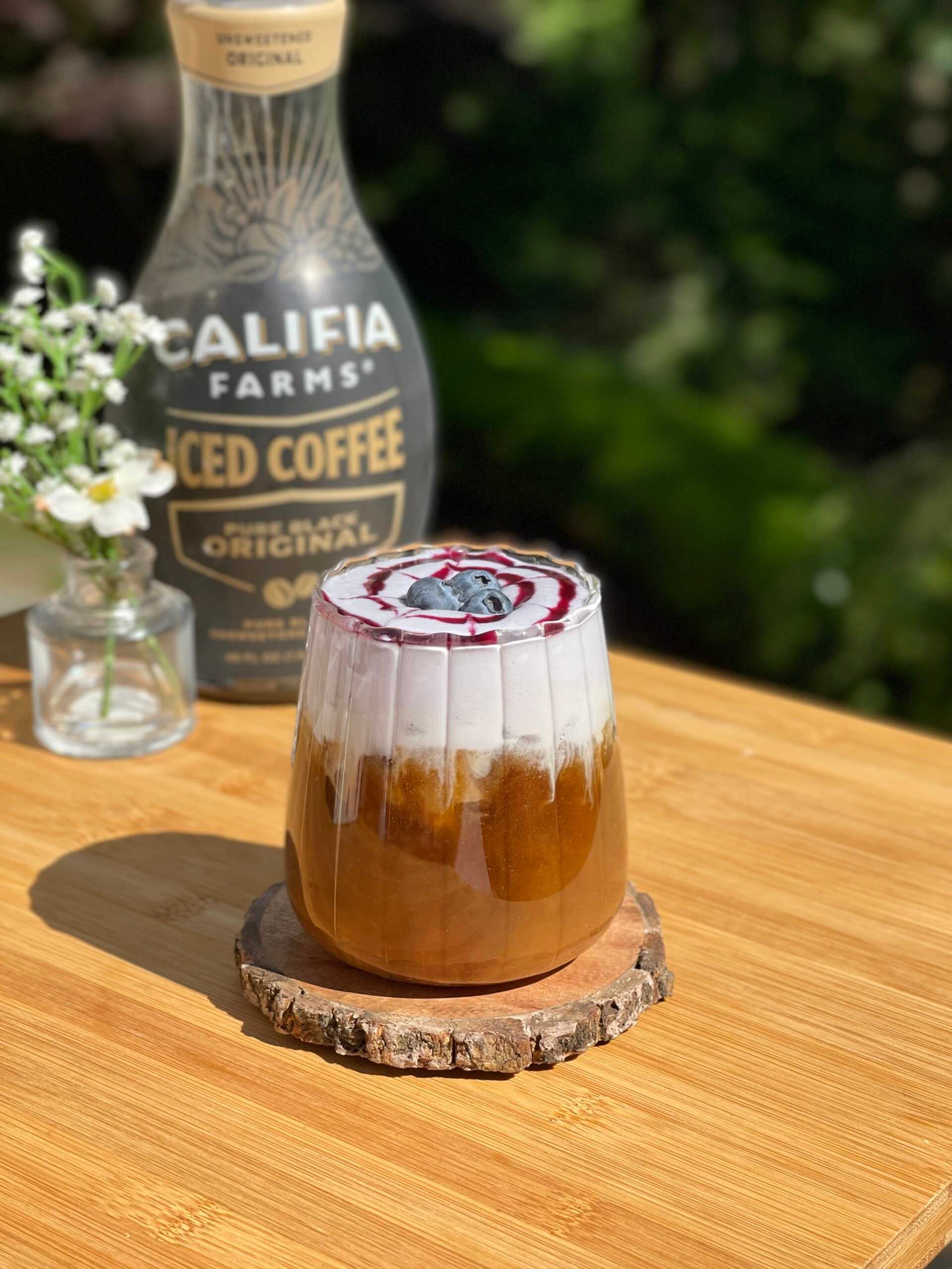 An iced coffee with blueberry cold foam sits in the center of the image, with Califia Farms Iced Coffee Original in the background.