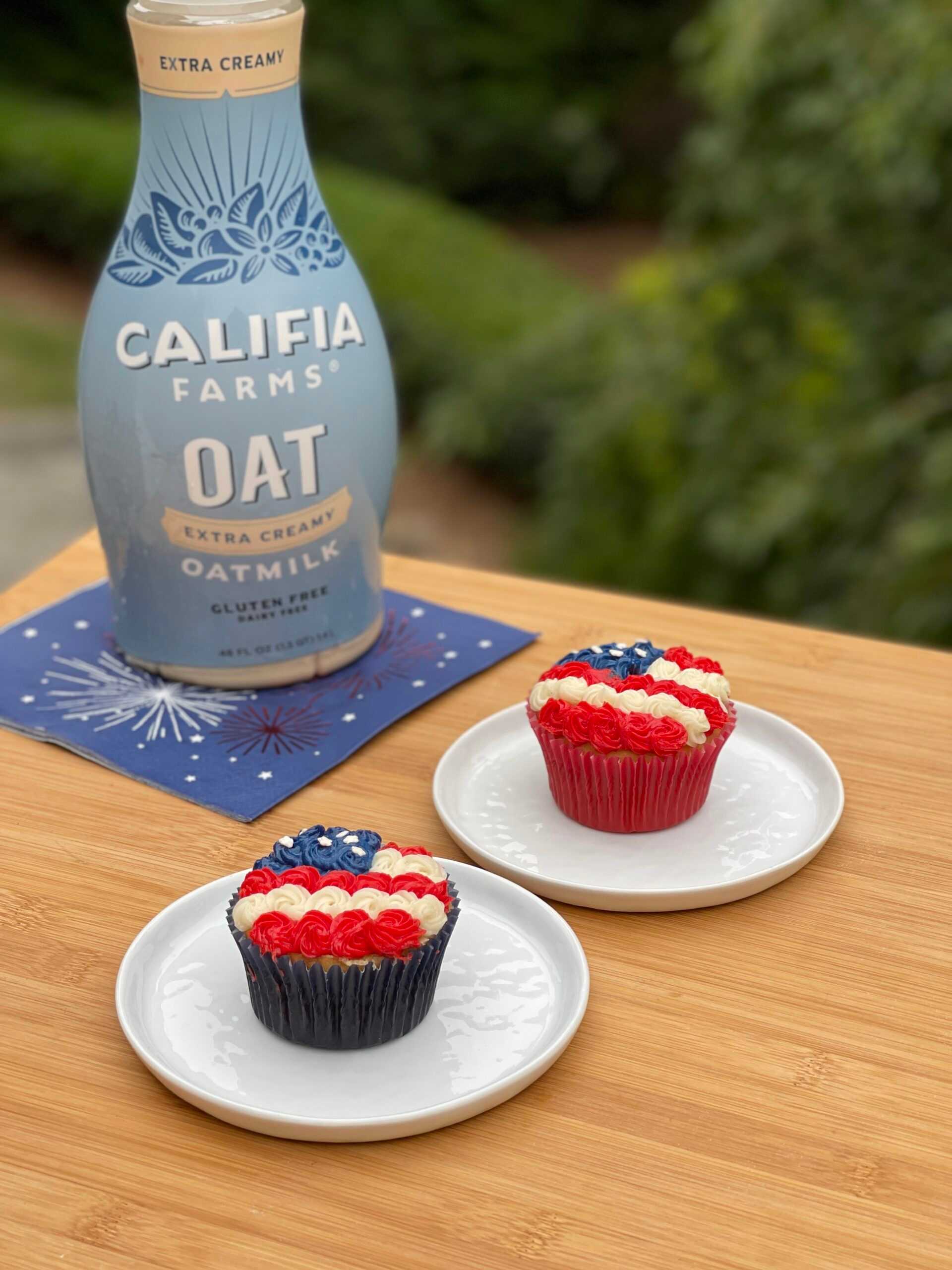 Two cupcakes decorated like the American flag sit at the center of the image, with Califia Farms Extra Creamy Oatmilk behind.