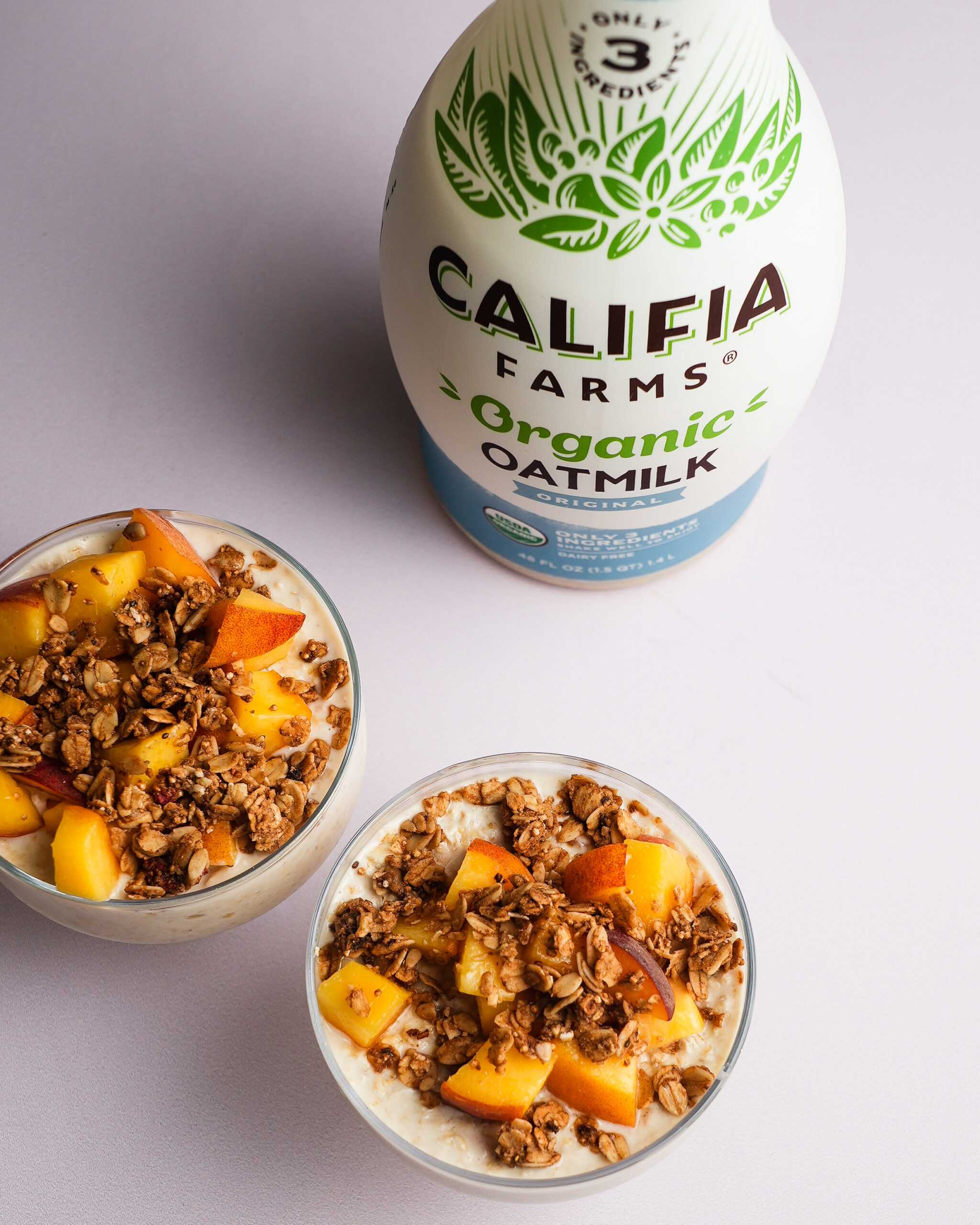 Overnight oats with peaches and granola topping sit in the front of the image, with Califia Farms Organic Oatmilk behind.