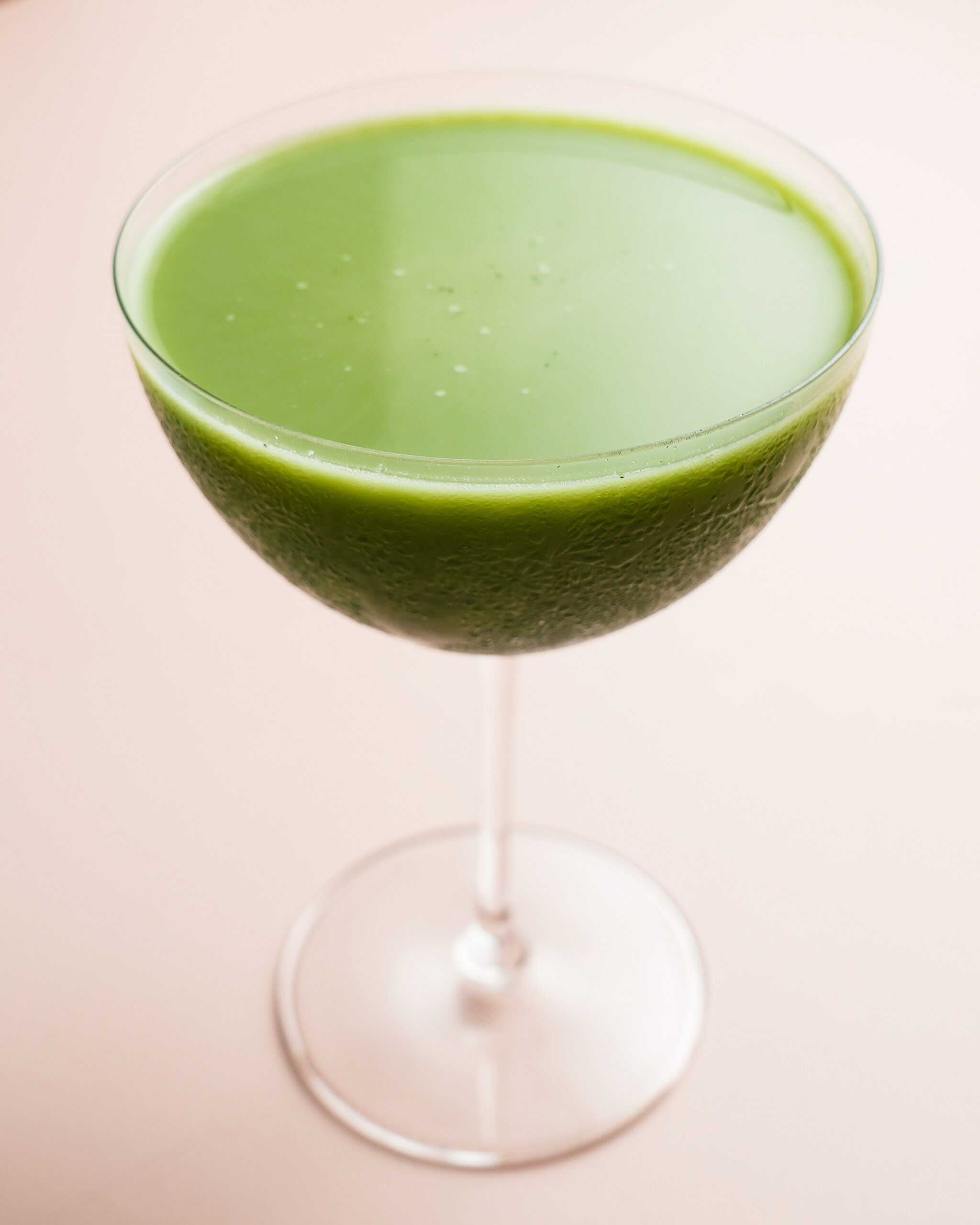 A bright green matcha martini in a martini glass sits in the center of the image.